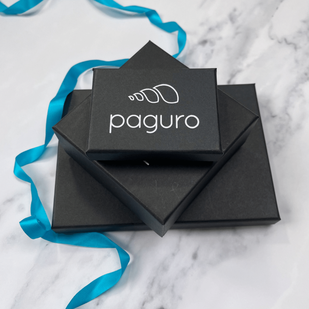 Paguro Upcycle black jewelry boxes stacked on marble surface with blue ribbon around for recycled rubber flower earrings