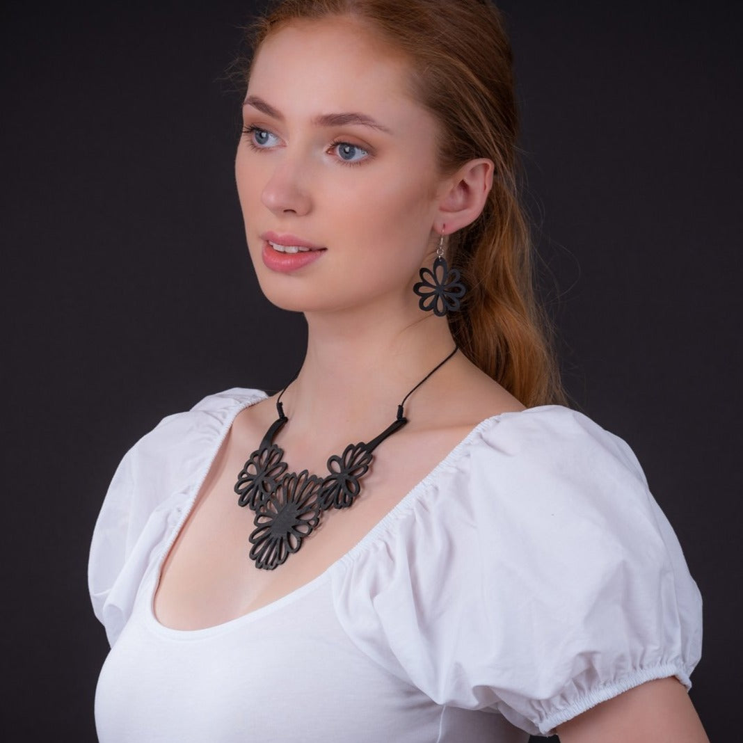 Woman wearing recycled rubber flower earrings and matching necklace by Paguro Upcycle