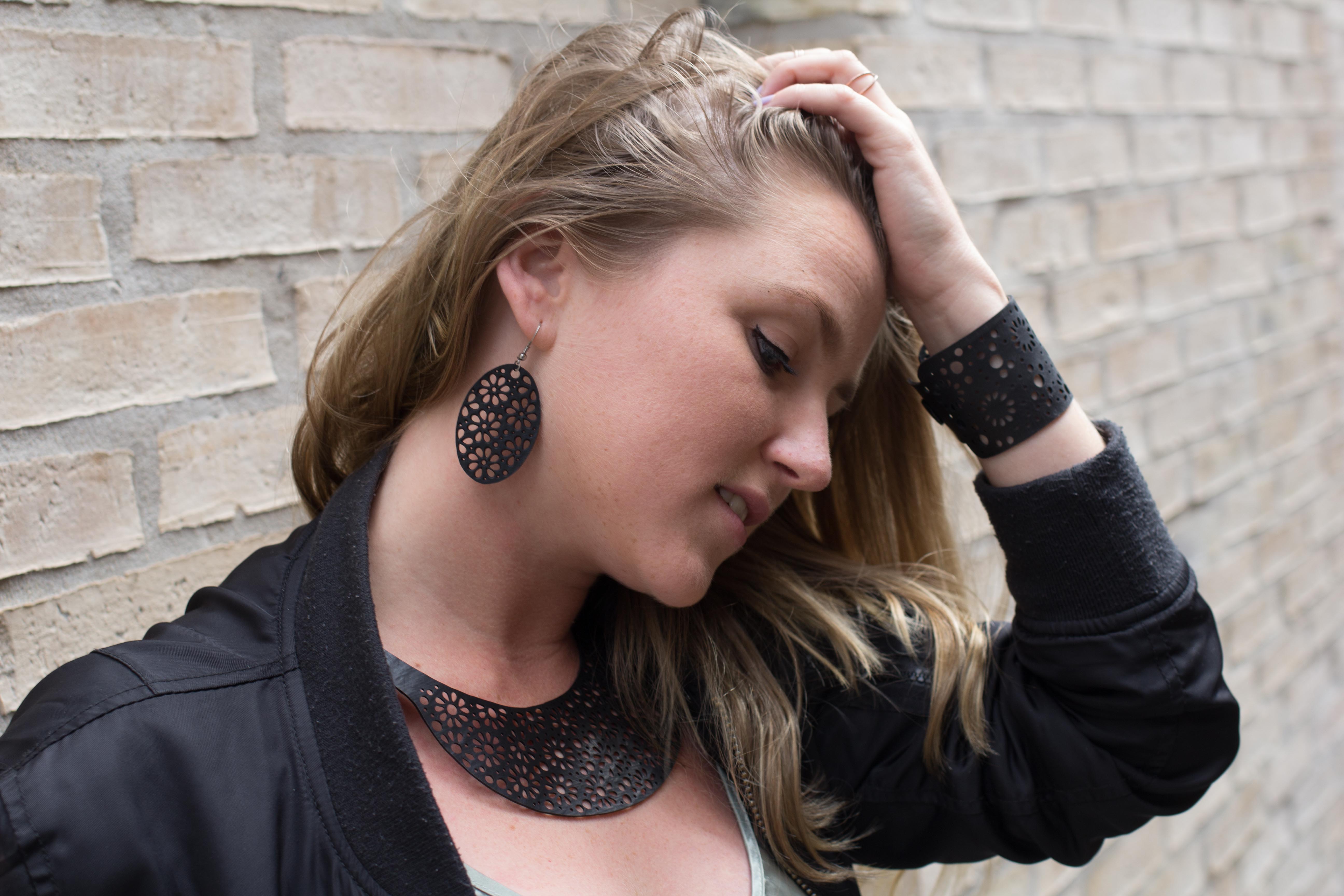 Paguro Upcycle recycled rubber bracelet on womans wrist with matching necklace and earrings against brick wall