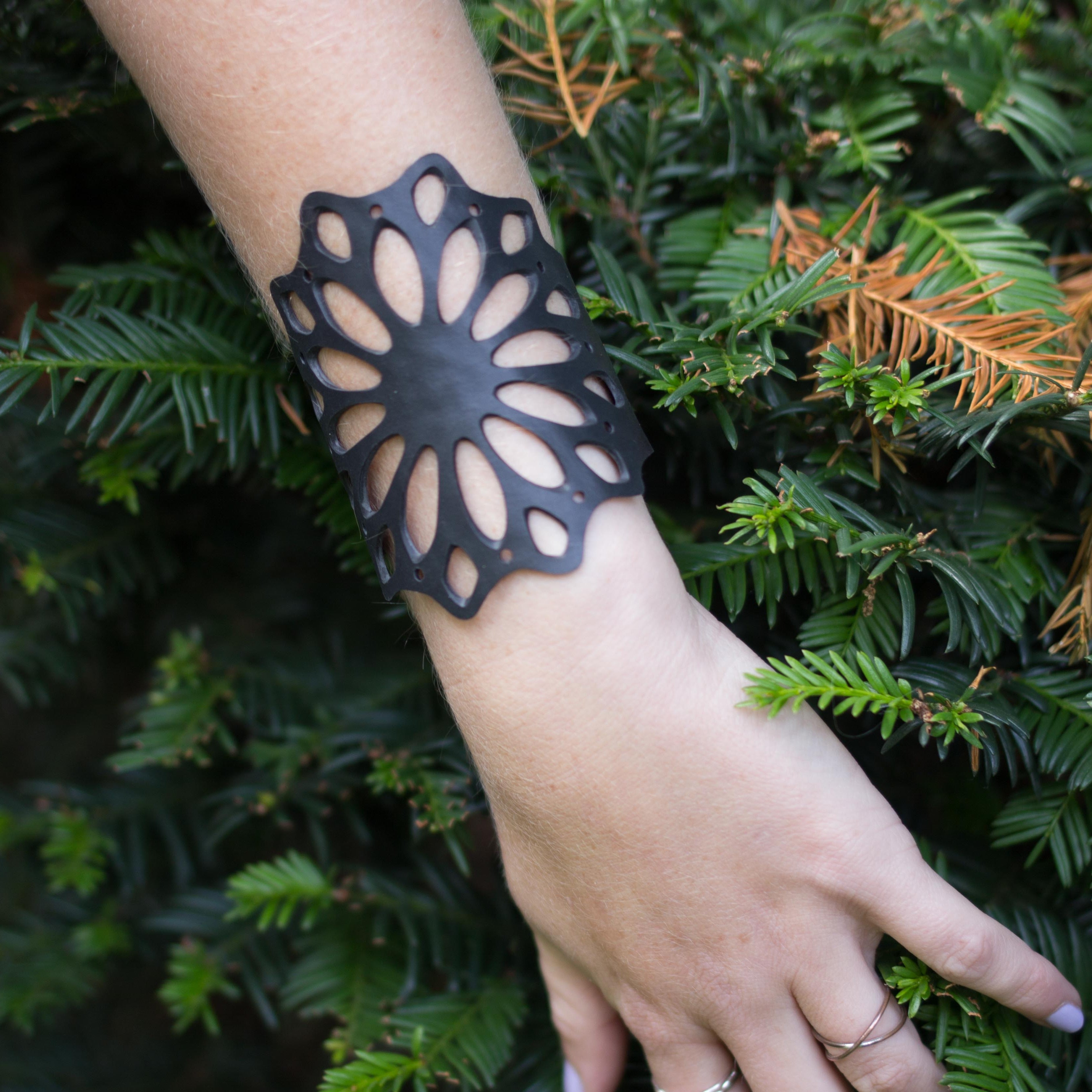 Paguro Upcycle black floral cutout cuff recycled rubber bracelet on wrist against green foliage