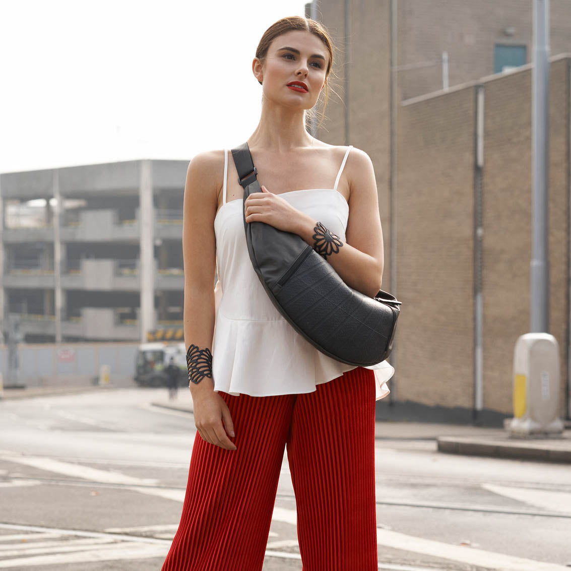 Woman wearing recycled rubber bracelet by Paguro Upcycle paired with white top and red pants outdoors