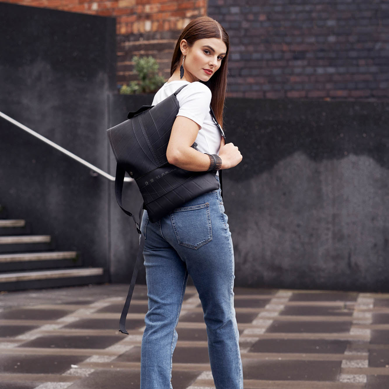 Model wearing Paguro Upcycle recycled rubber bracelet with black backpack in urban street style