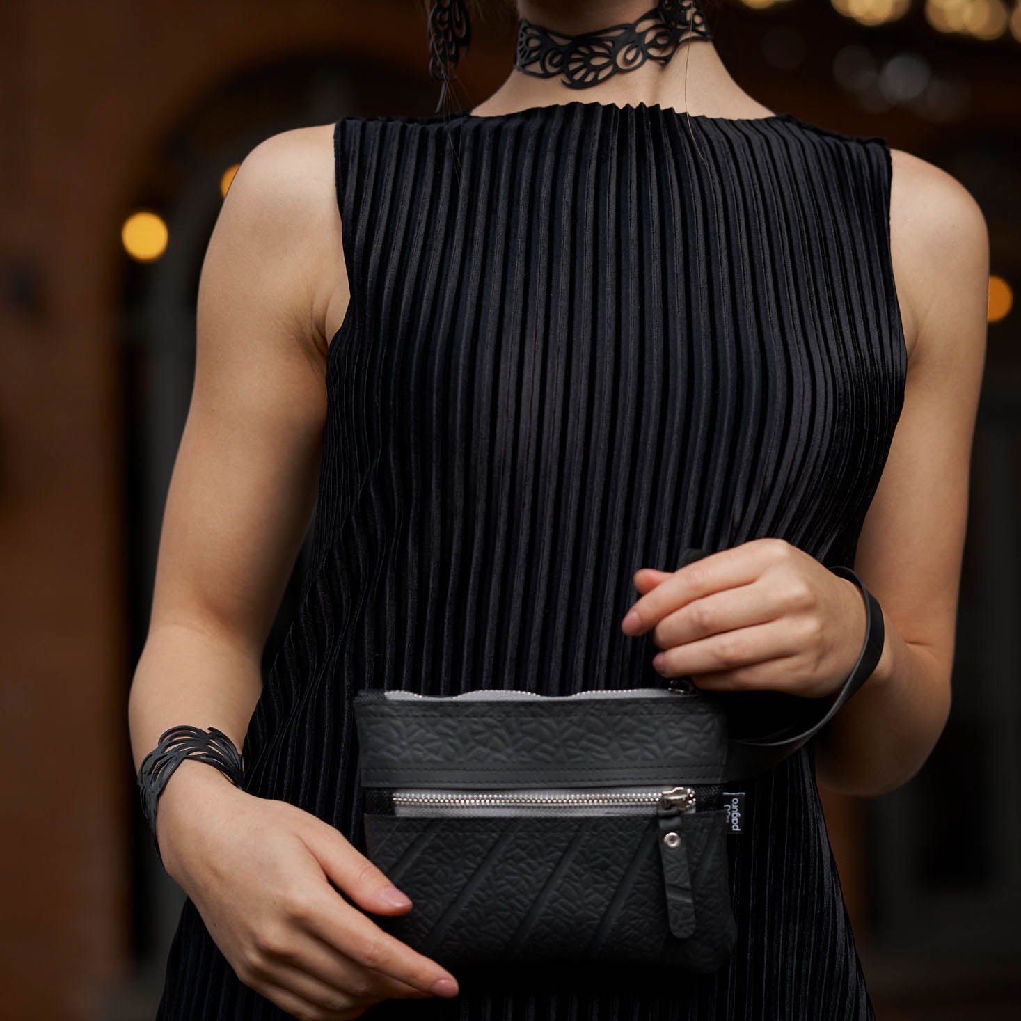 Paguro Upcycle black vegan wristlet pouch held by person wearing black dress and accessories